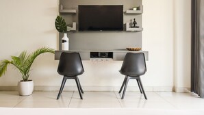 A modern living room with a flat-screen TV mounted on a grey wall, two black chairs, a potted plant, and a small shelf with decorative items. - Housr 1 RK Sector 27 Gurgaon Golf Course (Gurugram)