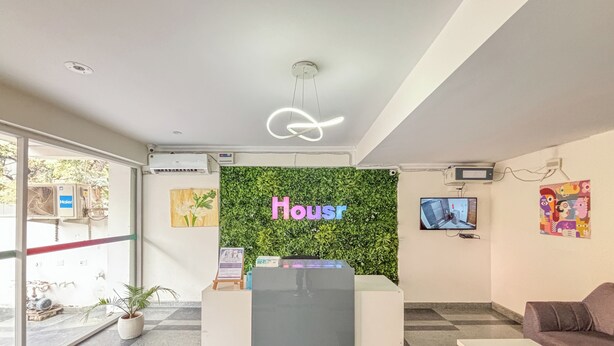 A modern hotel reception area with a green wall, a neon sign reading "Housr", and a reception desk. - Housr 1 RK Sector 27 Gurgaon Golf Course (Gurugram)
