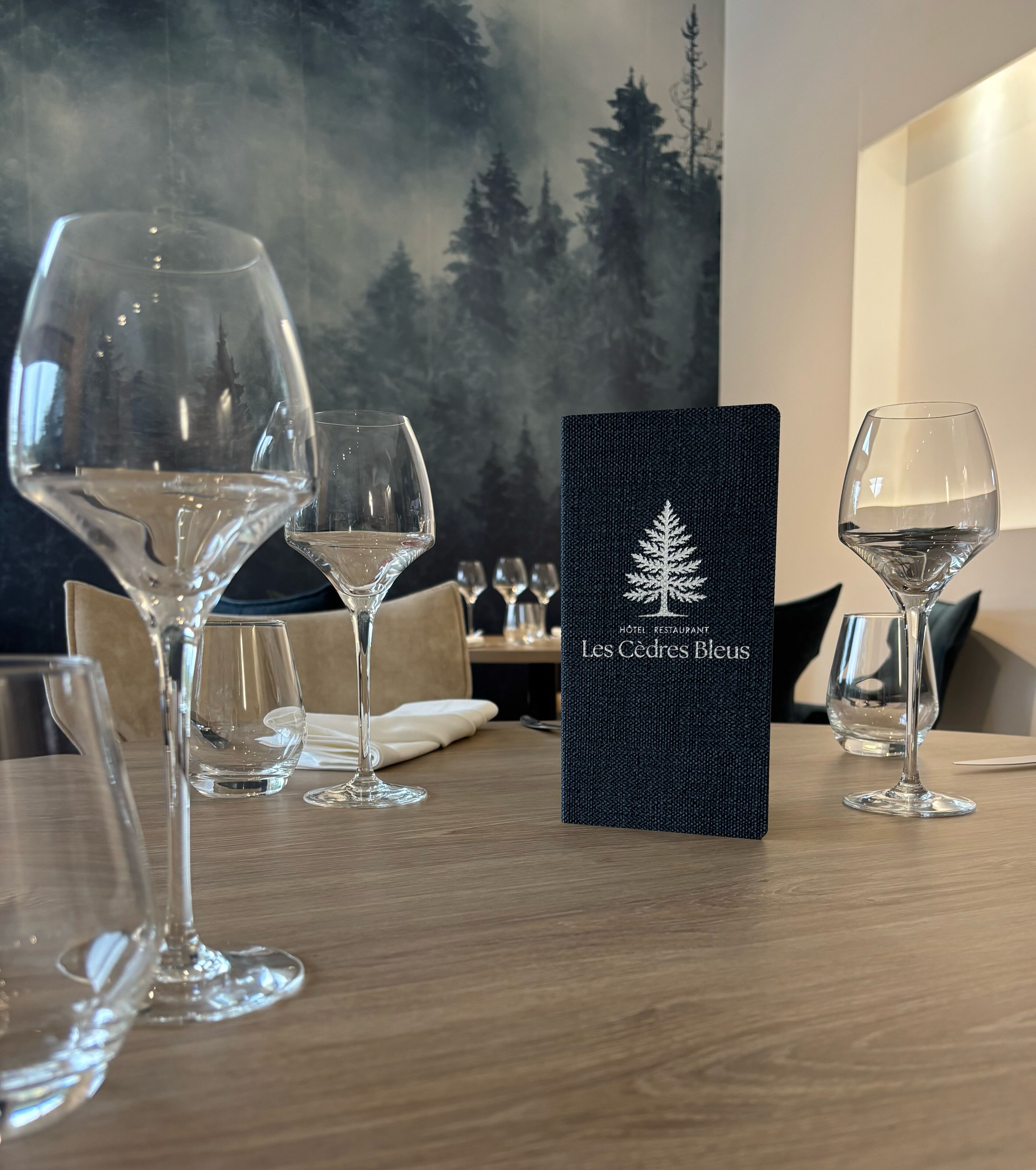 Une table avec plusieurs verres à vin vides et un menu noir orné d’un logo représentant un arbre, sur lequel on peut lire : « Les Cedres Bleus ».