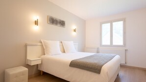 Une chambre à coucher avec un lit, des tables de chevet, une commode, un radiateur et une fenêtre.