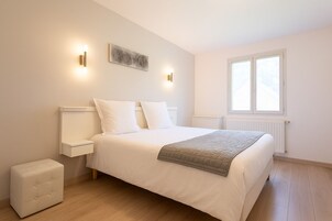 Un dormitorio con cama, mesitas de noche, un radiador y una ventana.
