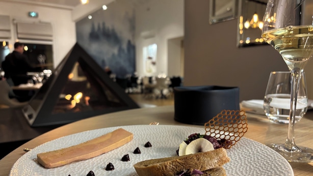Une assiette de desserts comprenant divers éléments, notamment une part de gâteau, du chocolat et une structure en forme de nid d’abeilles, accompagnée d’un verre de vin blanc.