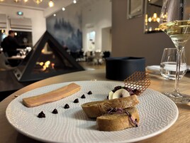 Un plato de postre con varios elementos, incluyendo un trozo de pastel, chocolate y una estructura de panal, acompañado de una copa de vino blanco.