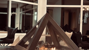 Un intérieur moderne avec une cheminée fermée par une paroi de verre, des fauteuils en cuir noir et de grandes fenêtres.