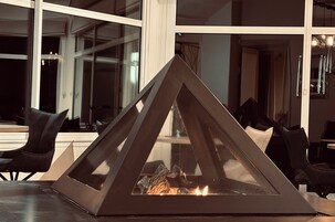 Un interior moderno con chimenea de cristal, sillones de cuero negro y ventanas amplias.