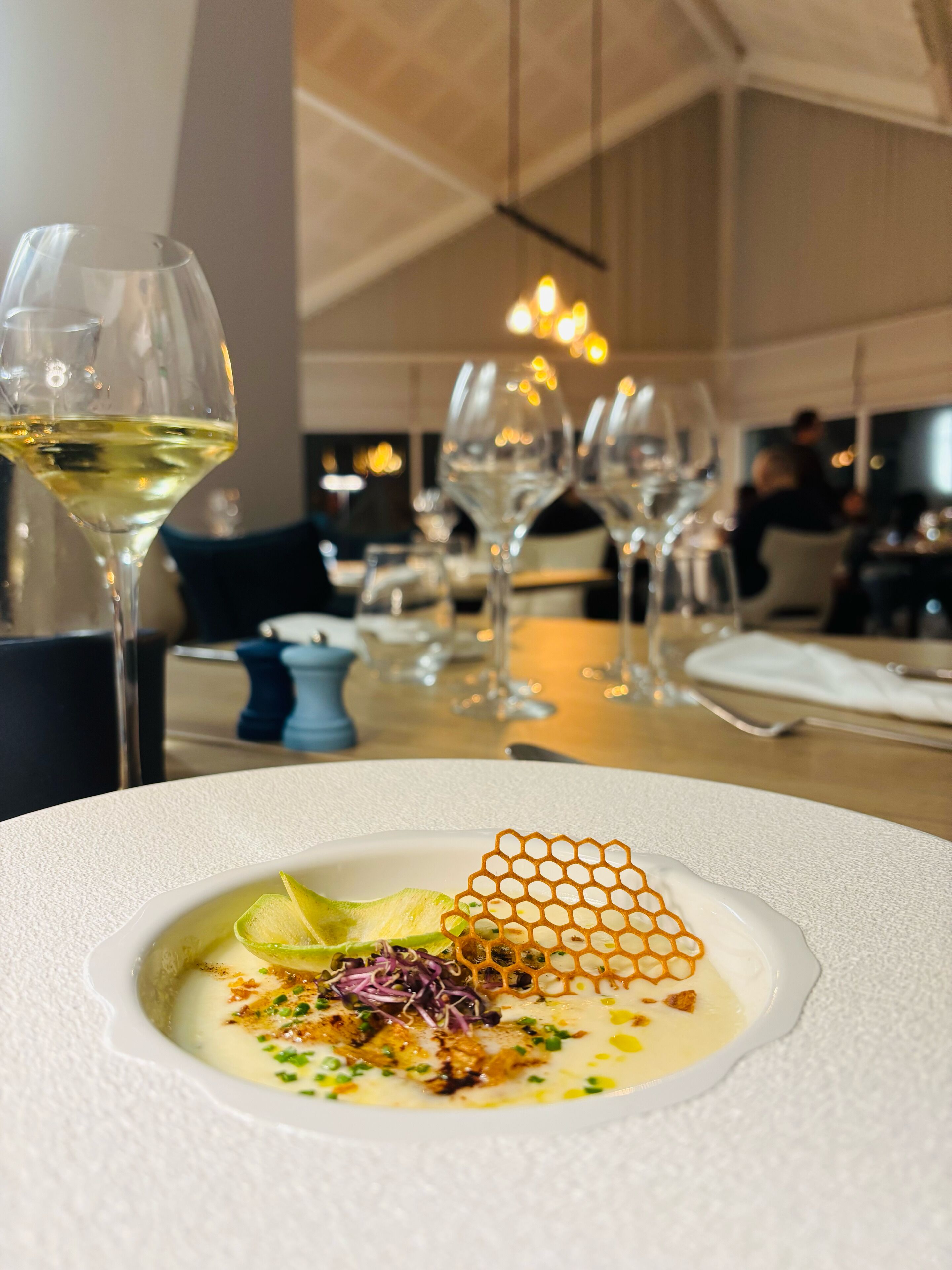 A dining table with a white plate of food, wine glasses, and a modern interior with hanging lights.