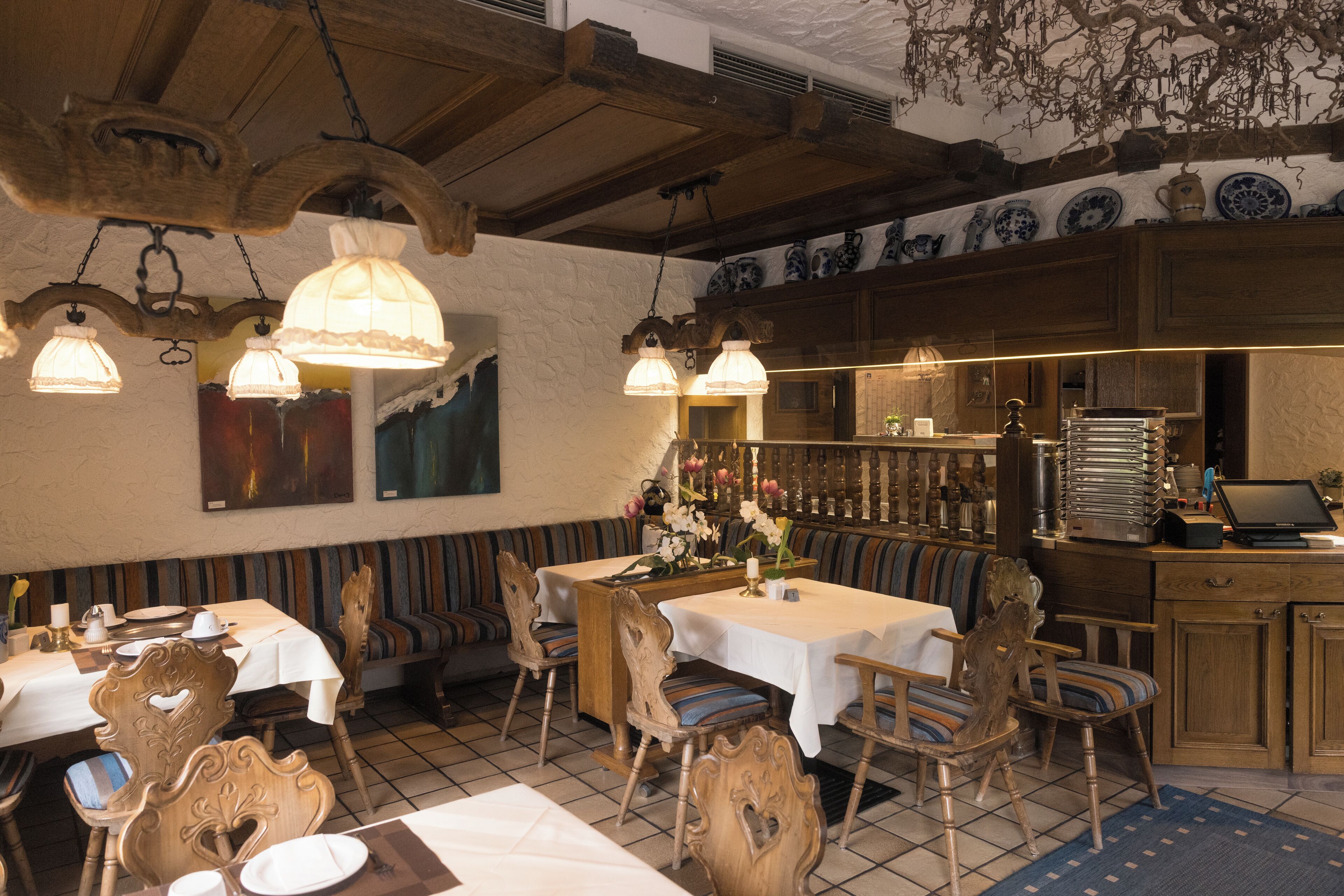 Un restaurante con mobiliario de madera, manteles blancos y lámparas colgantes.