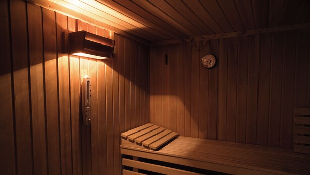 Eine Sauna mit Holzbänken und einem an der Wand montierten Ofen.