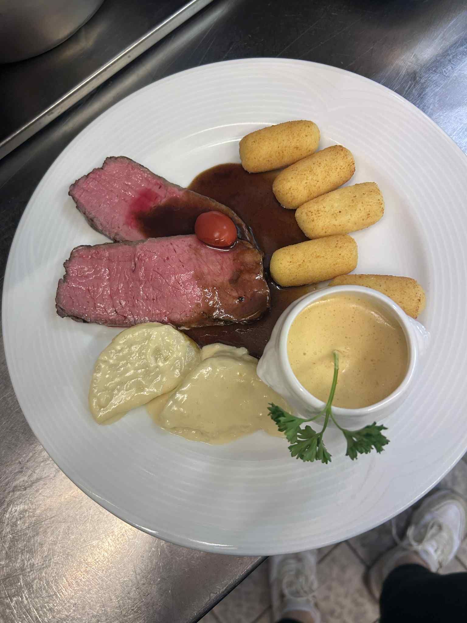 A plate with slices of beef, a small tomato, and a side of potato croquettes.