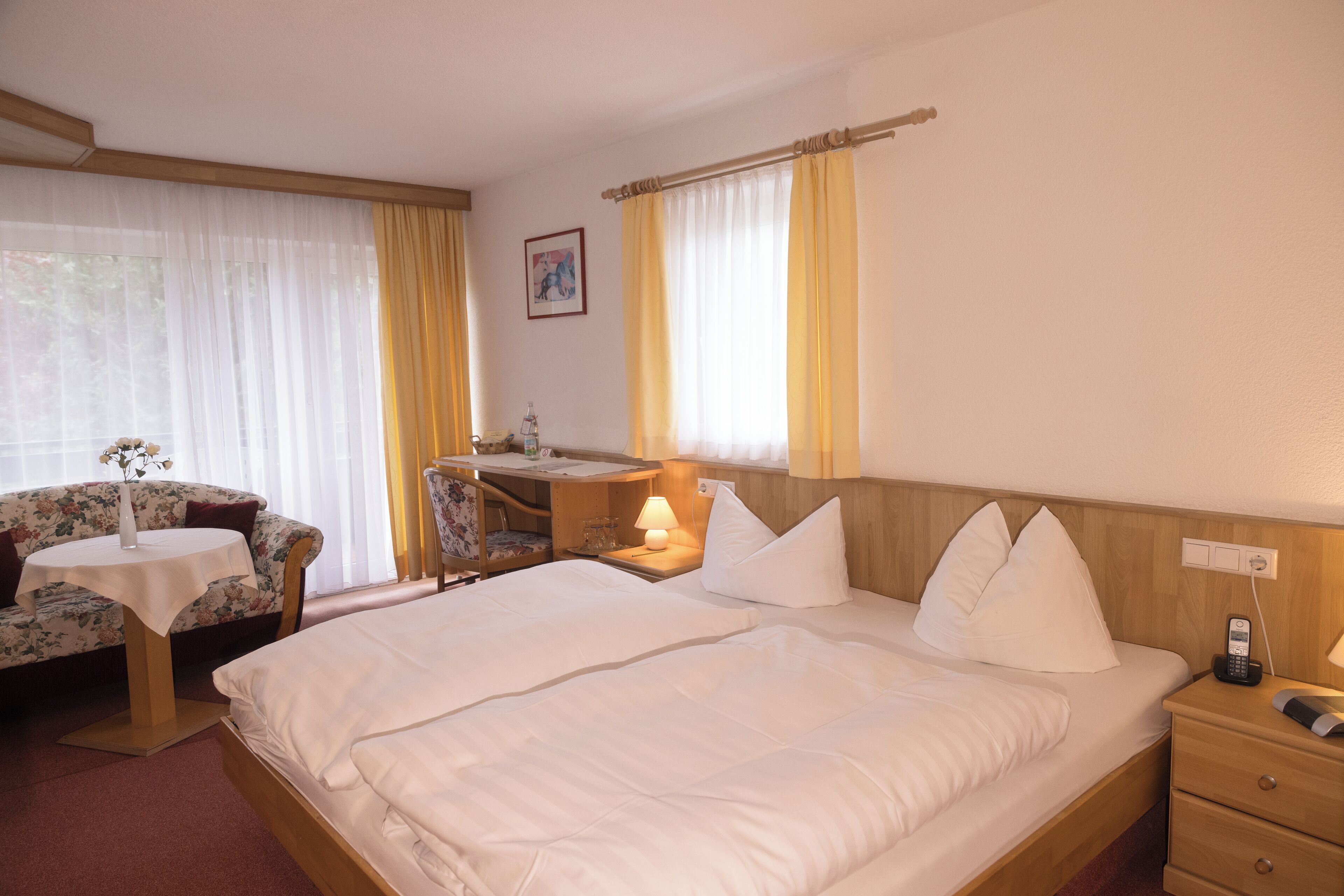 A hotel room with a large bed, a desk, a chair, and a small table with a vase.