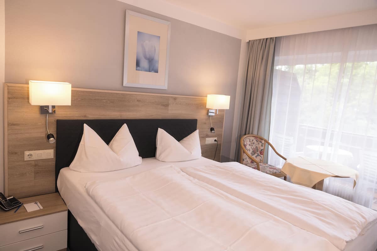 Una habitació d'hotel amb un llit gran, dues làmpades de nit, una cadira, una taula petita i una finestra amb cortines.