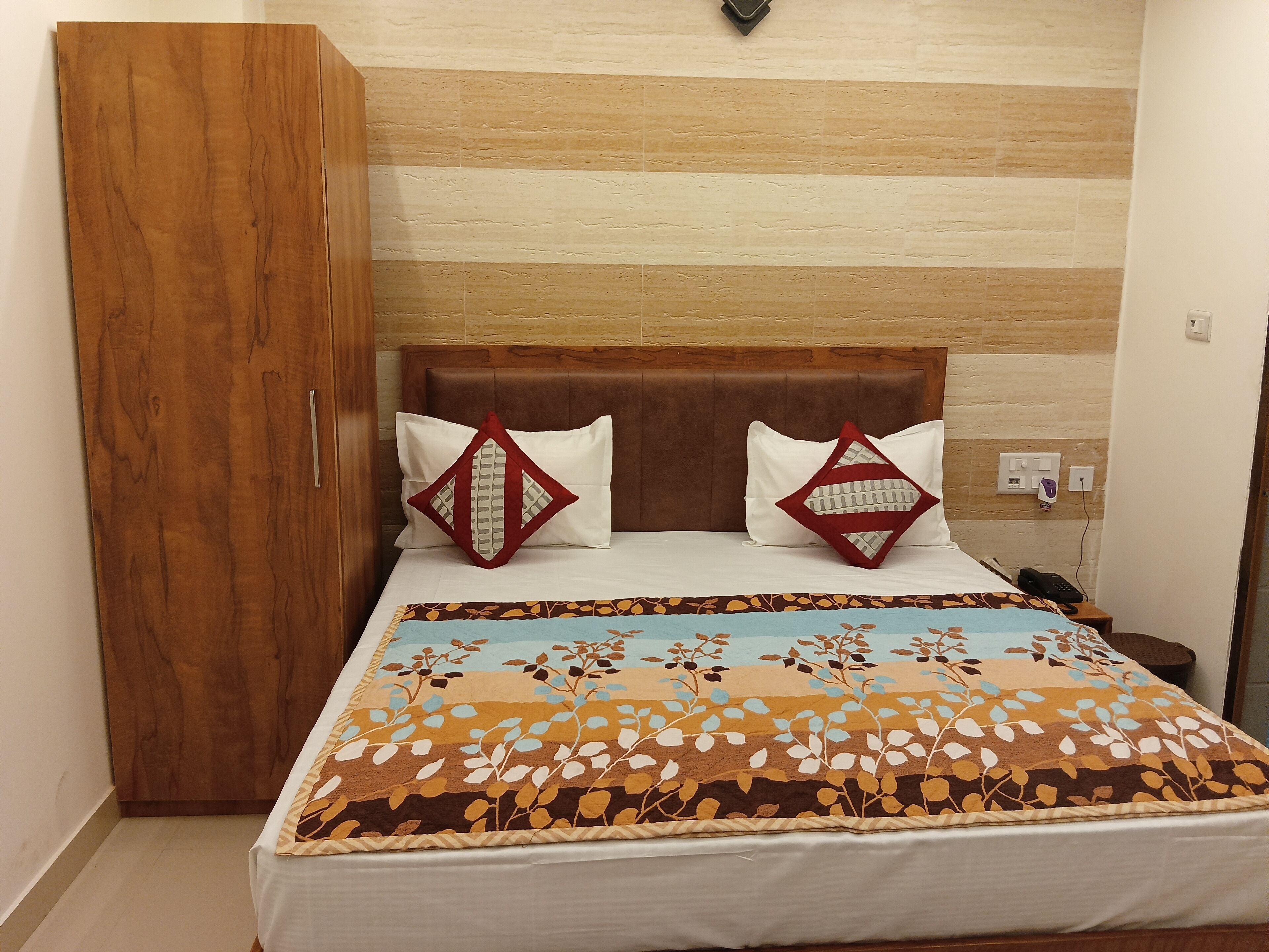 A bed with a patterned bedspread, two pillows with geometric designs, a wooden headboard, and a nightstand with a phone.
