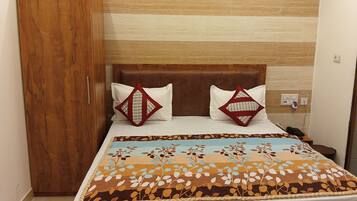 A bed with a patterned bedspread, two pillows with geometric designs, a wooden headboard, and a nightstand with a phone.