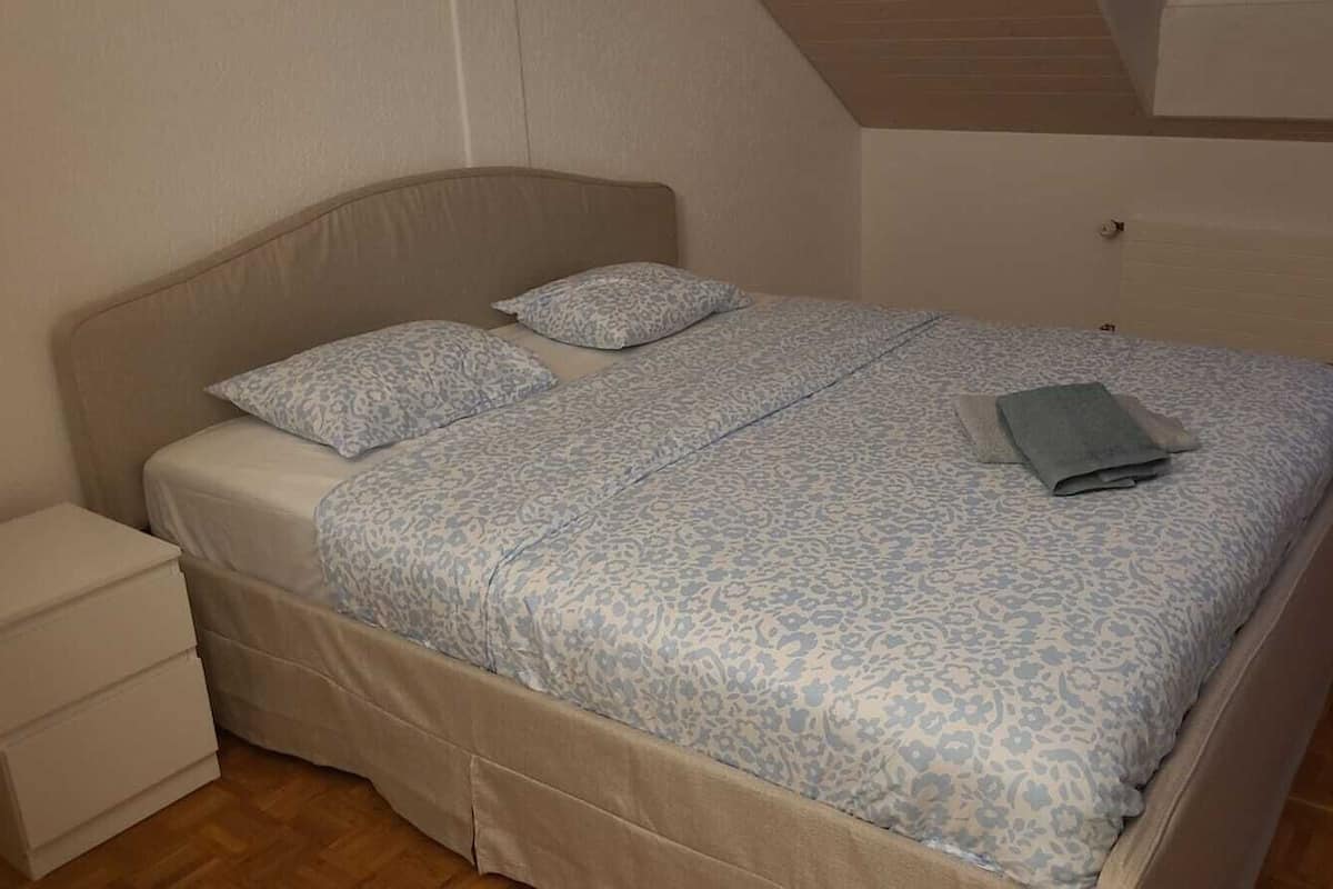 Ein Einzelbett mit gemustertem Bettbezug und Kissen, ein Nachttisch und ein Holzboden.