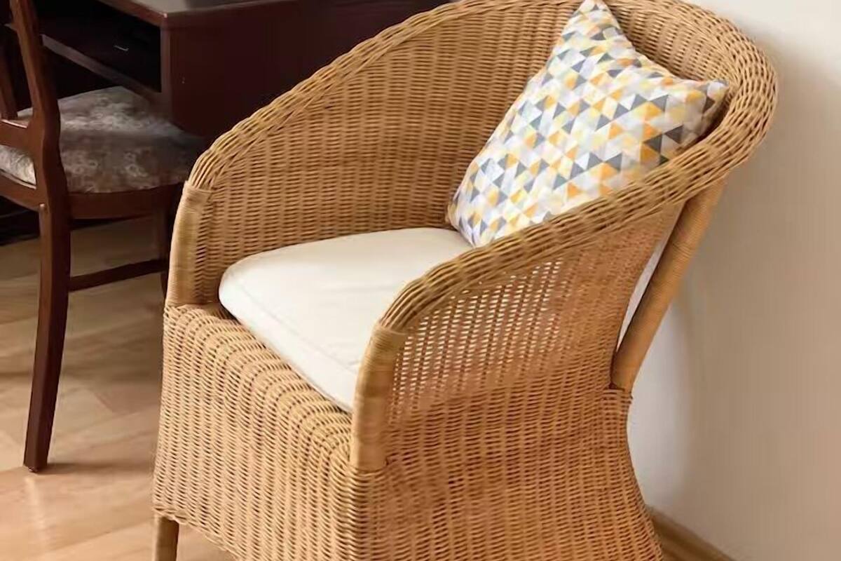 A wicker chair with a cushion and a geometric pillow, a desk with a computer, and a framed picture on the wall.
