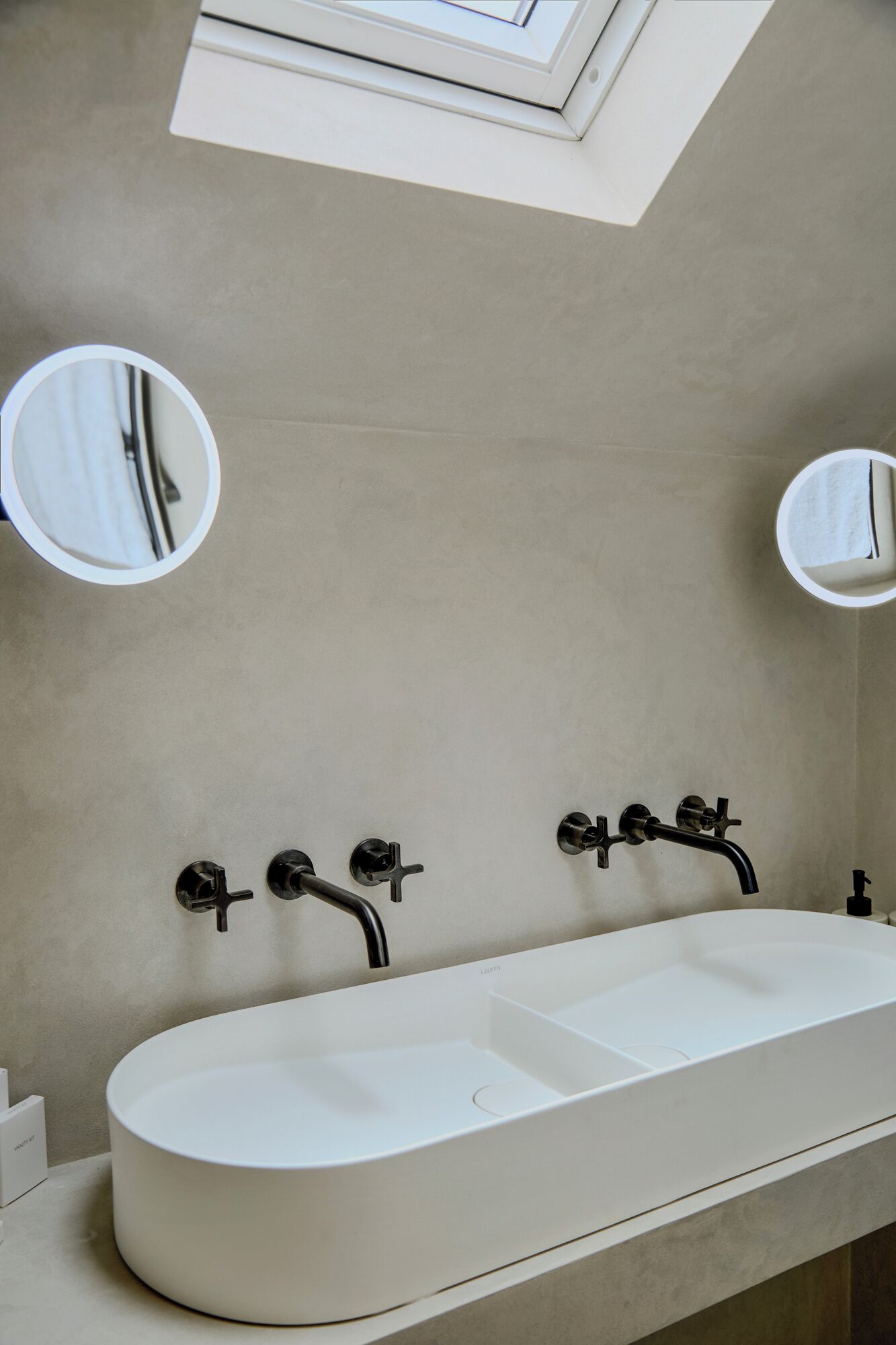 Une salle de bain moderne avec un grand lavabo ovale, deux robinets et deux miroirs fixés au mur.