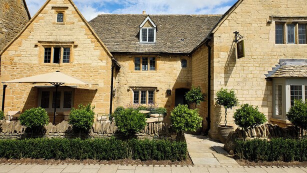 A stone building with a covered patio, outdoor seating, and neatly trimmed hedges. - House of George W. Davies (Broadway)