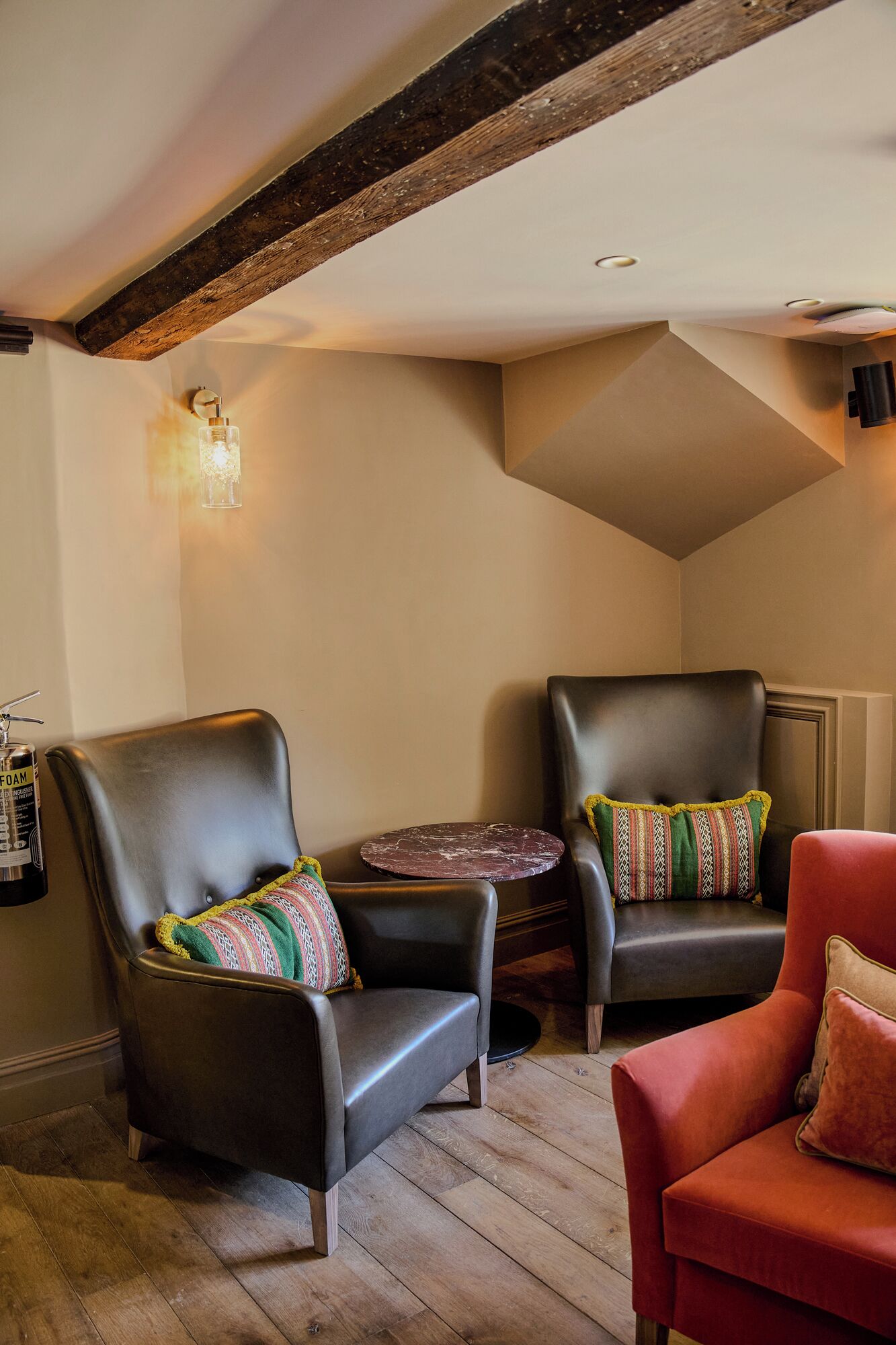 A cozy corner with two leather armchairs, a small round table, and a red chair.