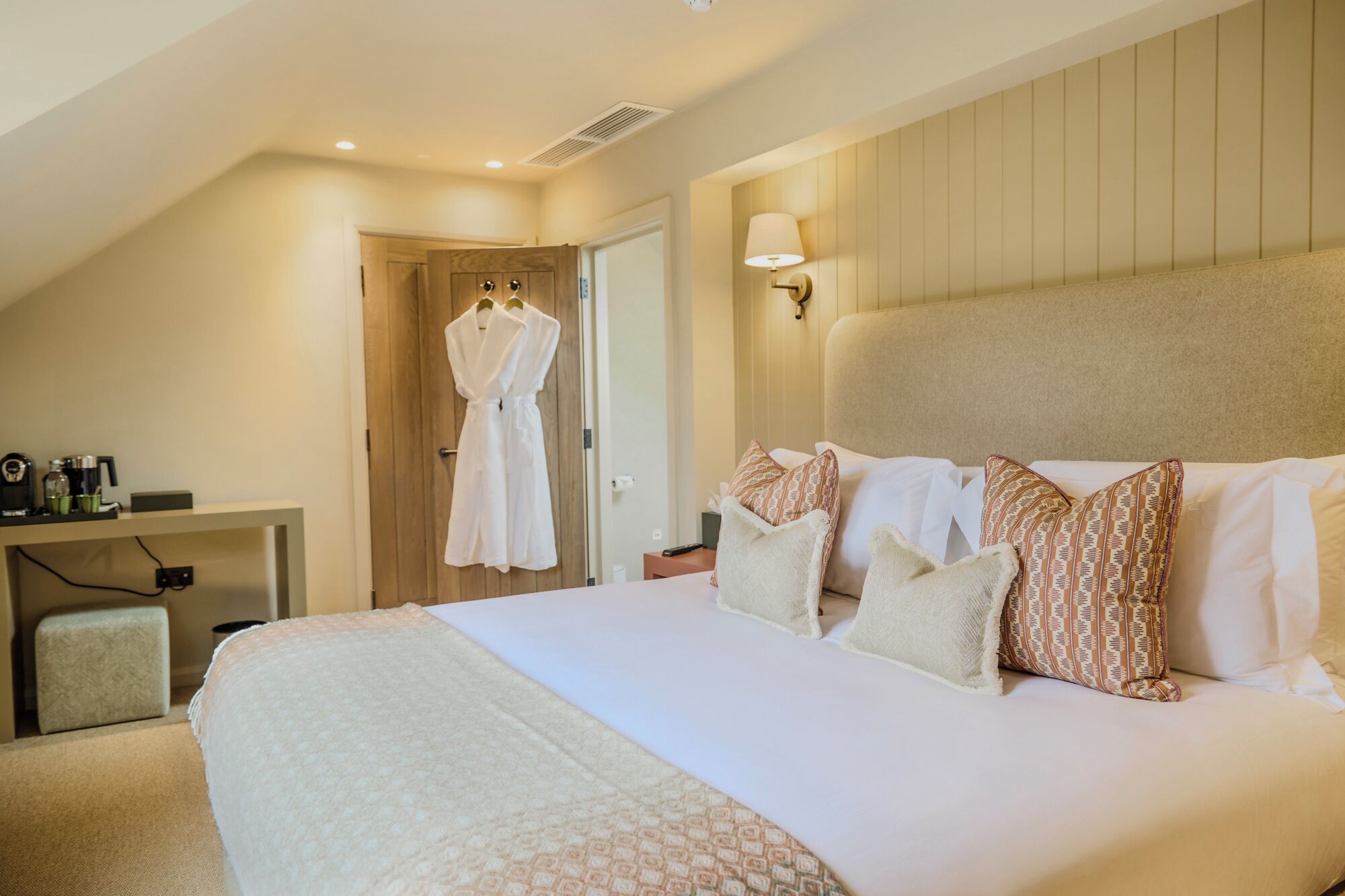 Habitación de hotel con una cama grande, una mesita de noche, una bata colgada en la puerta y una lámpara en la pared.