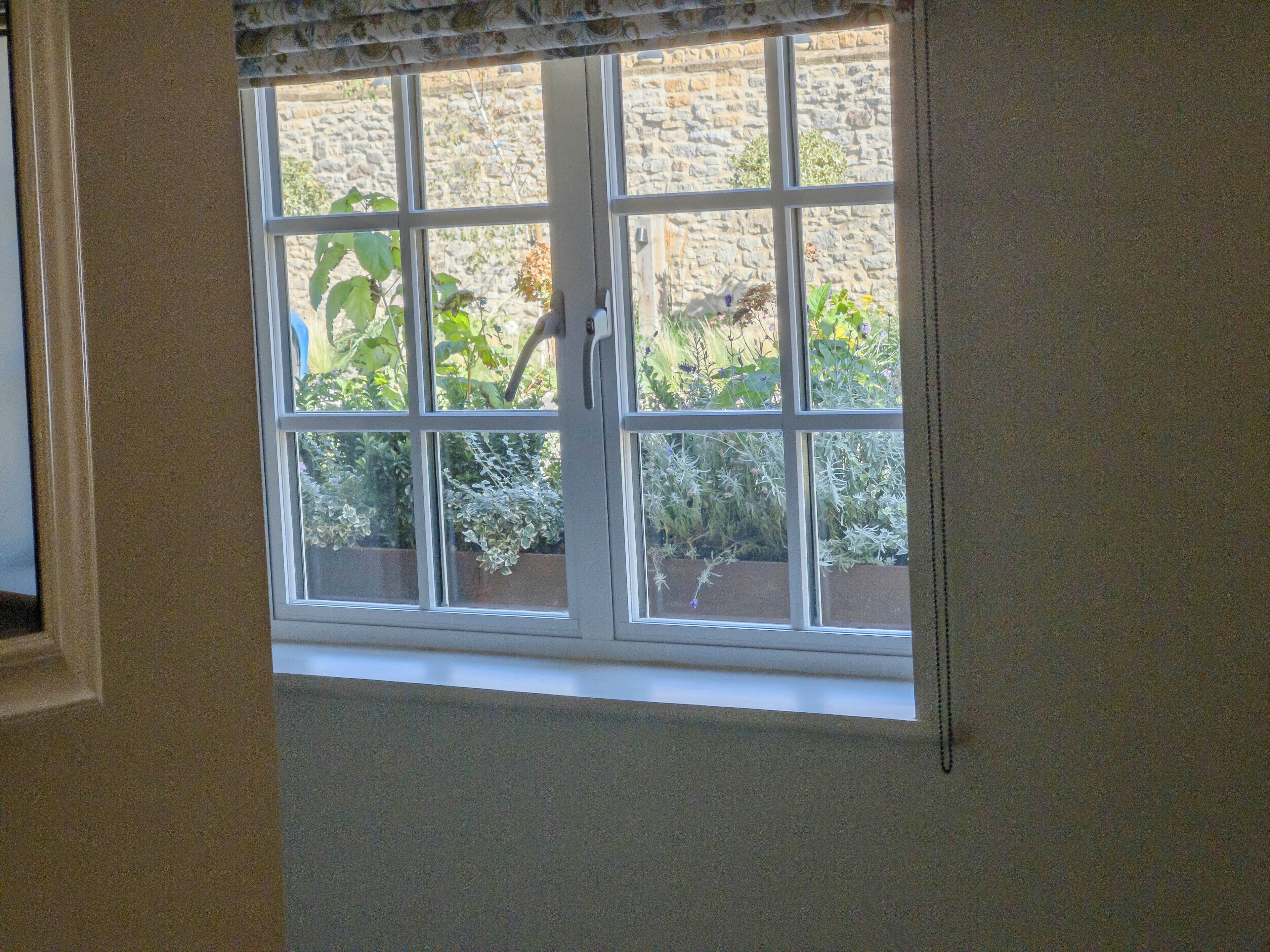 A window with a view of a stone wall and greenery outside.