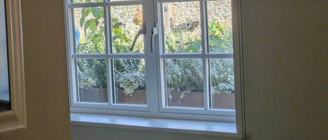 A window with a view of a stone wall and greenery outside.