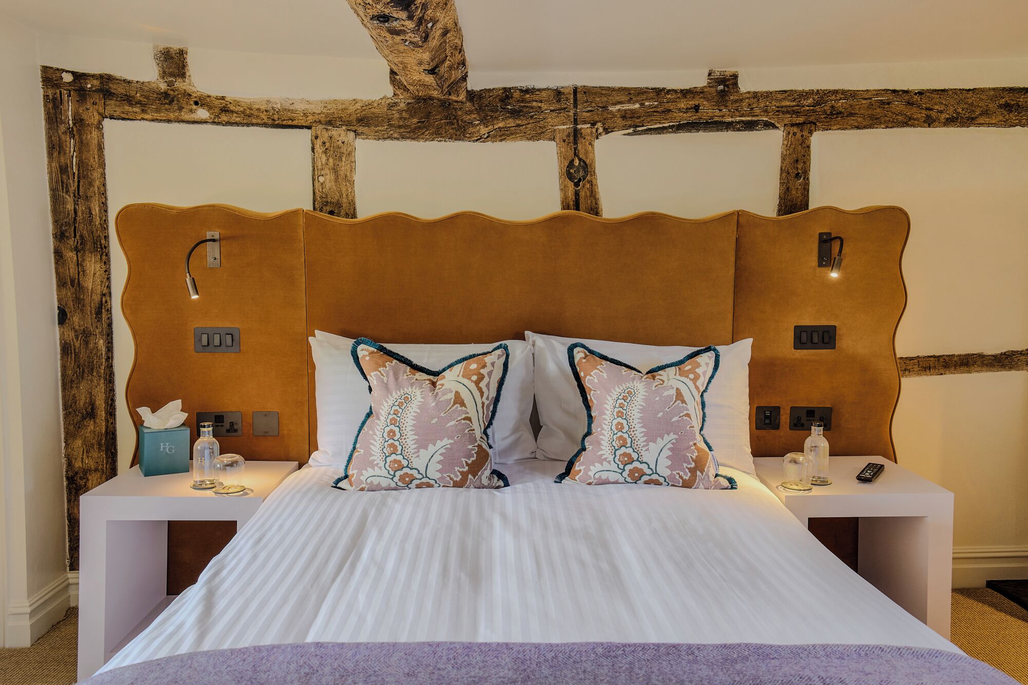 A bed with a wooden headboard, two bedside tables, and a nightstand with a lamp and a bottle.