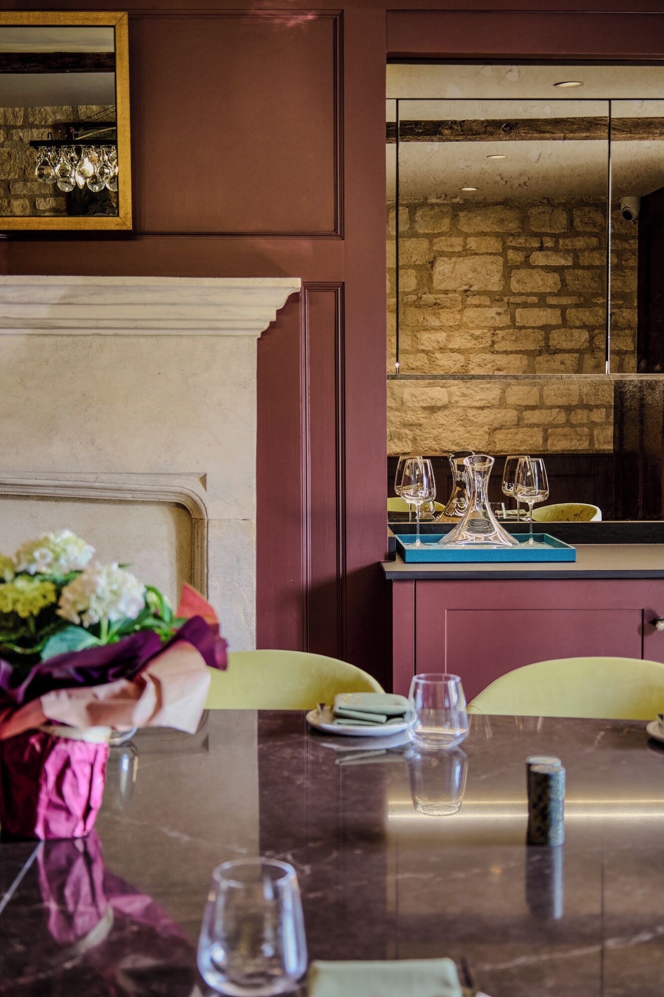 A dining area with a marble table, chairs, and a vase of flowers. A mirror reflects part of the room.