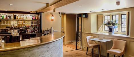 A bar area with a marble countertop, shelves of liquor bottles, and a seating area with two chairs and a table.