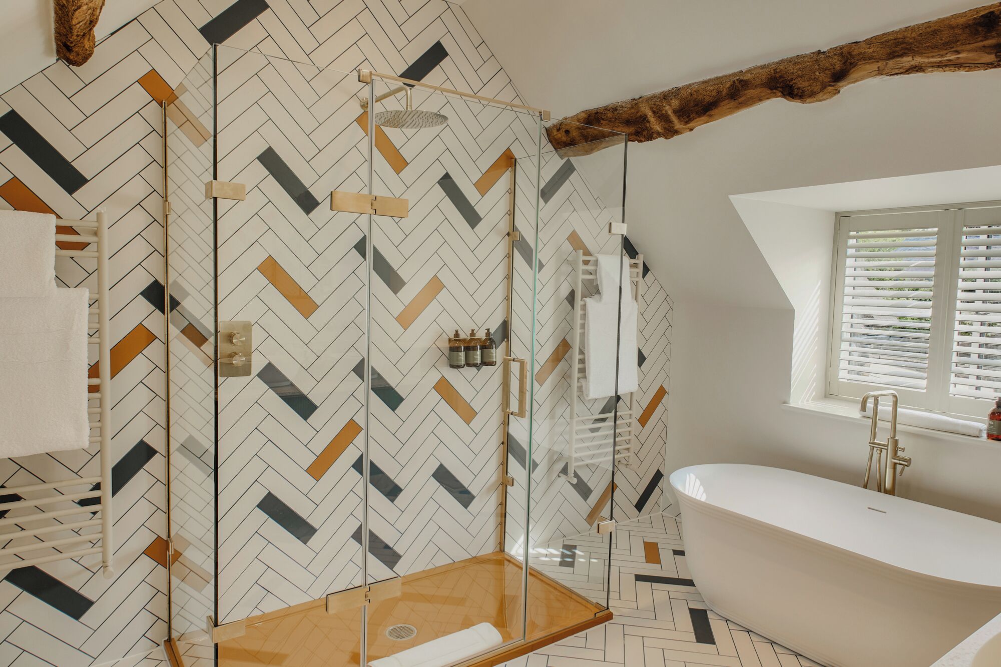 Un baño moderno con una bañera independiente, un box de ducha de cristal y suelo con estampado de espiga.