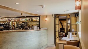A bar area with a curved counter, multiple shelves stocked with bottles, and a seating area with round tables and chairs. - House of George W. Davies (Broadway)