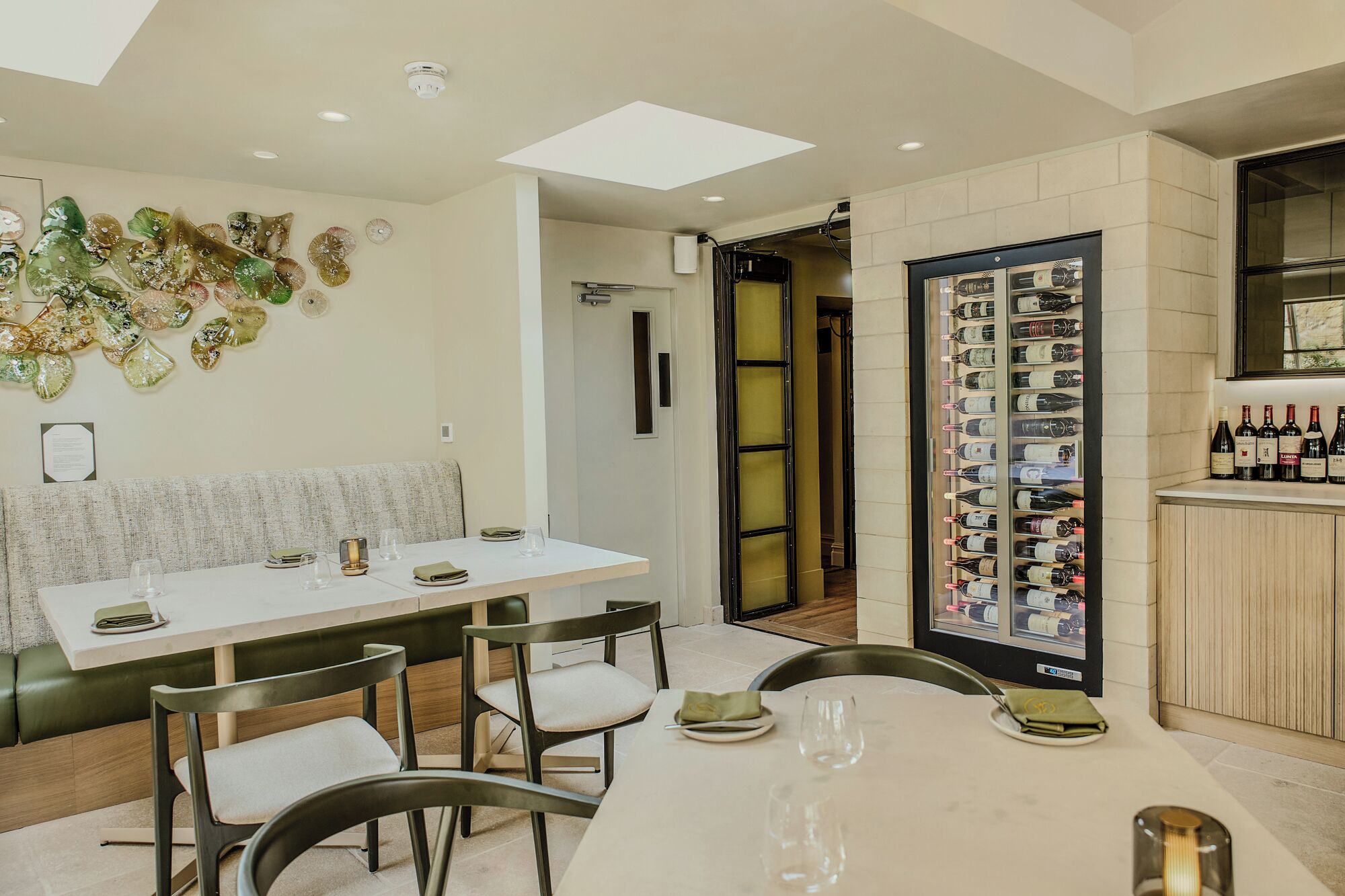 A dining area with a white table, green cushioned chairs, and a wine rack with bottles.