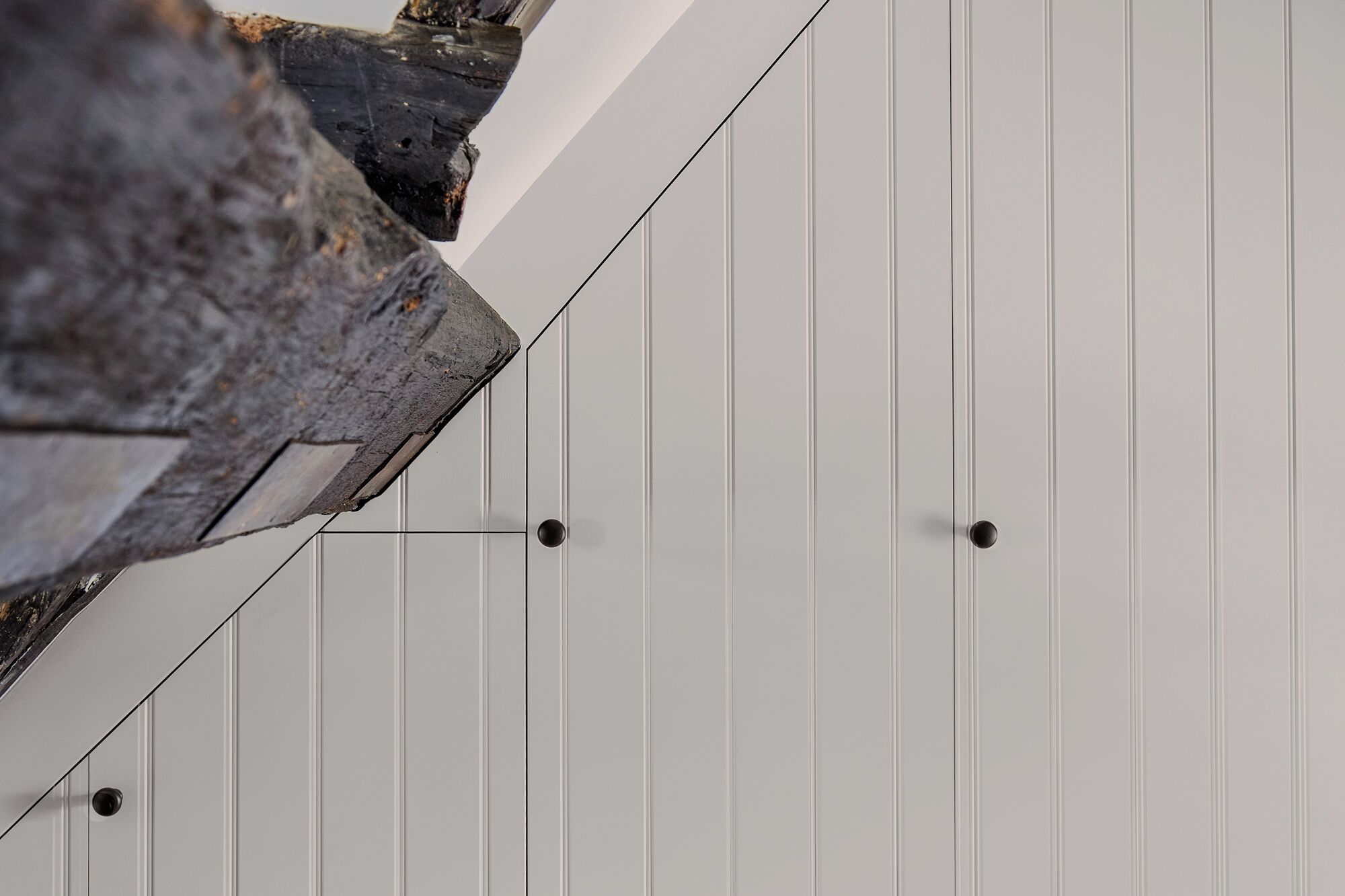 Primer plano de una pared blanca con paneles verticales y dos objetos circulares negros.