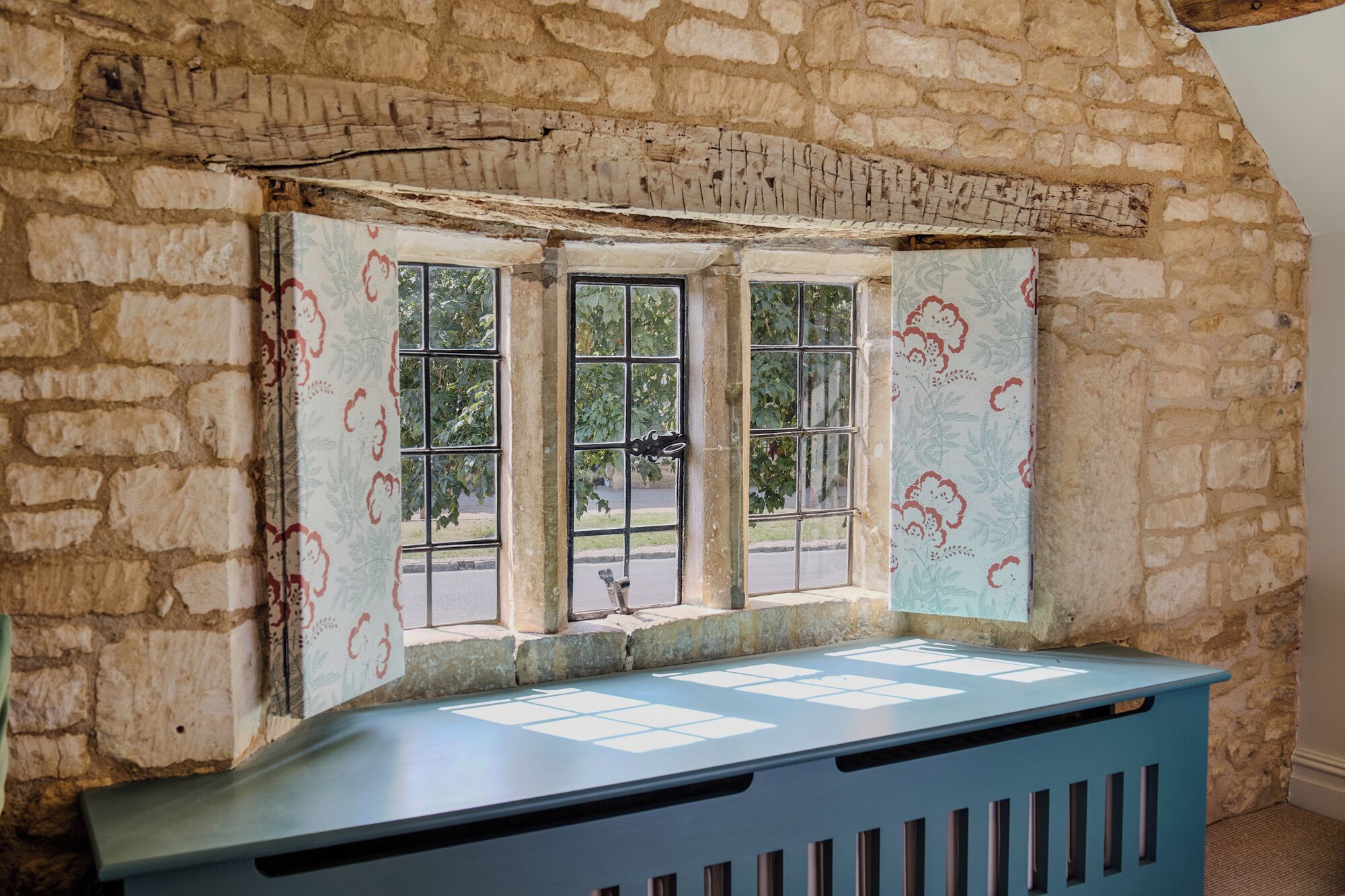 A room with a stone wall, a window with a metal grille, and a blue bench.