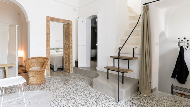 A spacious room with a large bed, a wicker chair, a staircase, and a coat rack. - Terrazza Costa by Wonderful Italy (Ostuni)