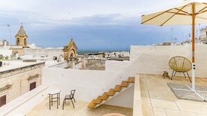 A rooftop terrace with a view of the city, a small table and chair, and a large umbrella. - Terrazza Costa by Wonderful Italy (Ostuni)