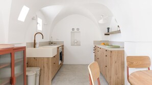 A modern kitchen with wooden cabinets, a built-in oven, and a sink. There is a small window above the sink and a shelf with kitchen items. - Terrazza Costa by Wonderful Italy (Ostuni)