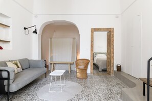 Ein modernes Wohnzimmer mit einem grauen Sofa, einem weißen Couchtisch, einem Korbstuhl und einem großen Spiegel.
