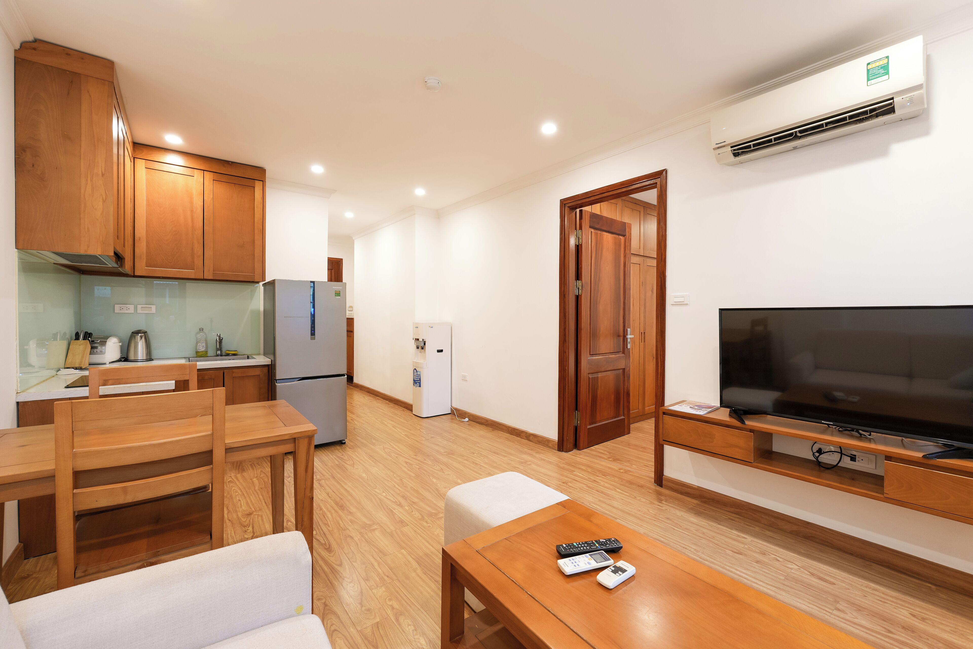 A compact living space with a kitchenette, wooden furniture, a flat-screen TV, and a built-in air conditioning unit.