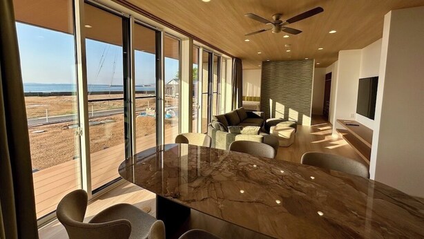 Uma área de jantar moderna com uma grande mesa de vidro, assentos confortáveis e vista para a praia.