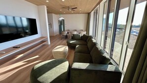 Ett modernt vardagsrum med en stor platt-TV, en hörnsoffa, ett soffbord och en matplats med ett högt bord och stolar.