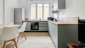 Una cocina moderna con una mesa de madera, sillas blancas, un horno empotrado y un ventanal grande.