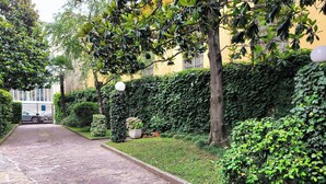 Un sendero empedrado que conduce a un edificio de fachada amarilla, rodeado de abundante vegetación y un seto.