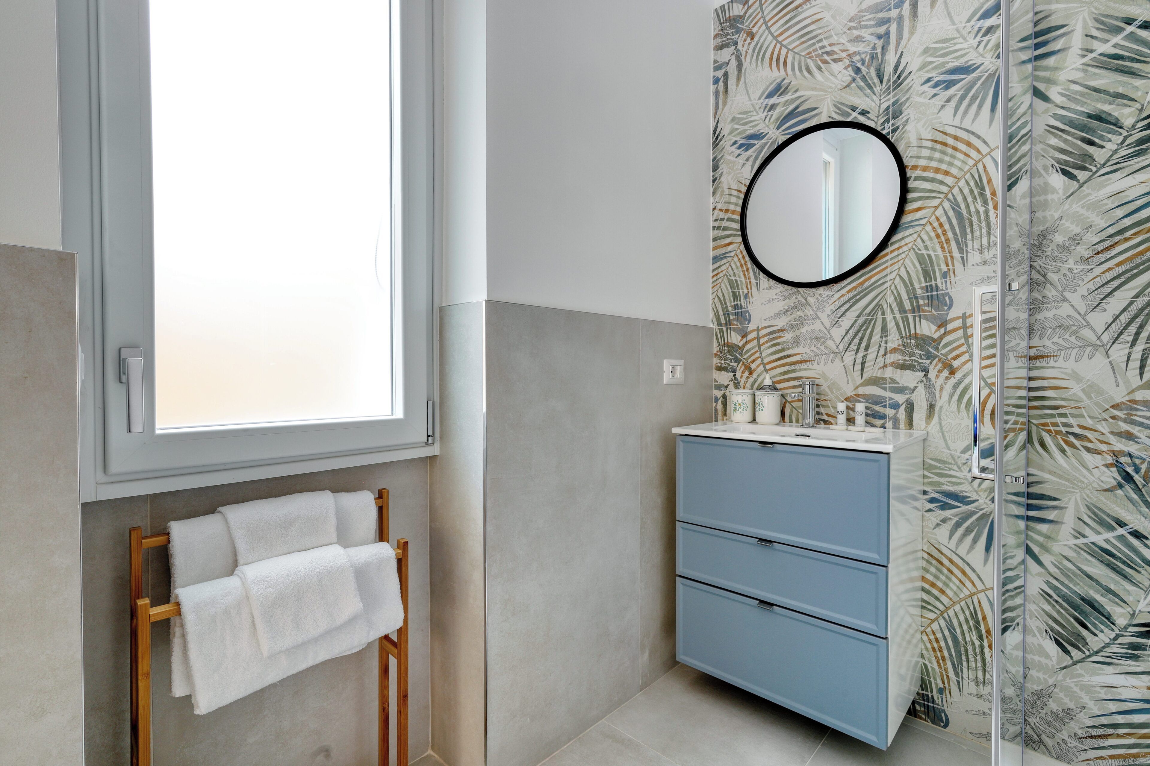Une salle de bain avec une fenêtre, un porte-serviettes, un miroir et un meuble-lavabo avec des tiroirs.