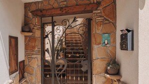 Une porte d’entrée en pierre avec un portail en métal, un pot de fleurs et une boîte aux lettres.