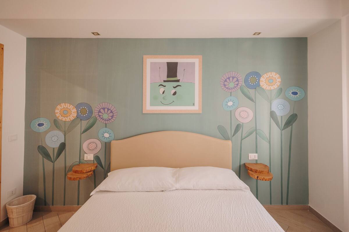 A bedroom with a bed, a wall mural of flowers, and a framed picture above the bed.
