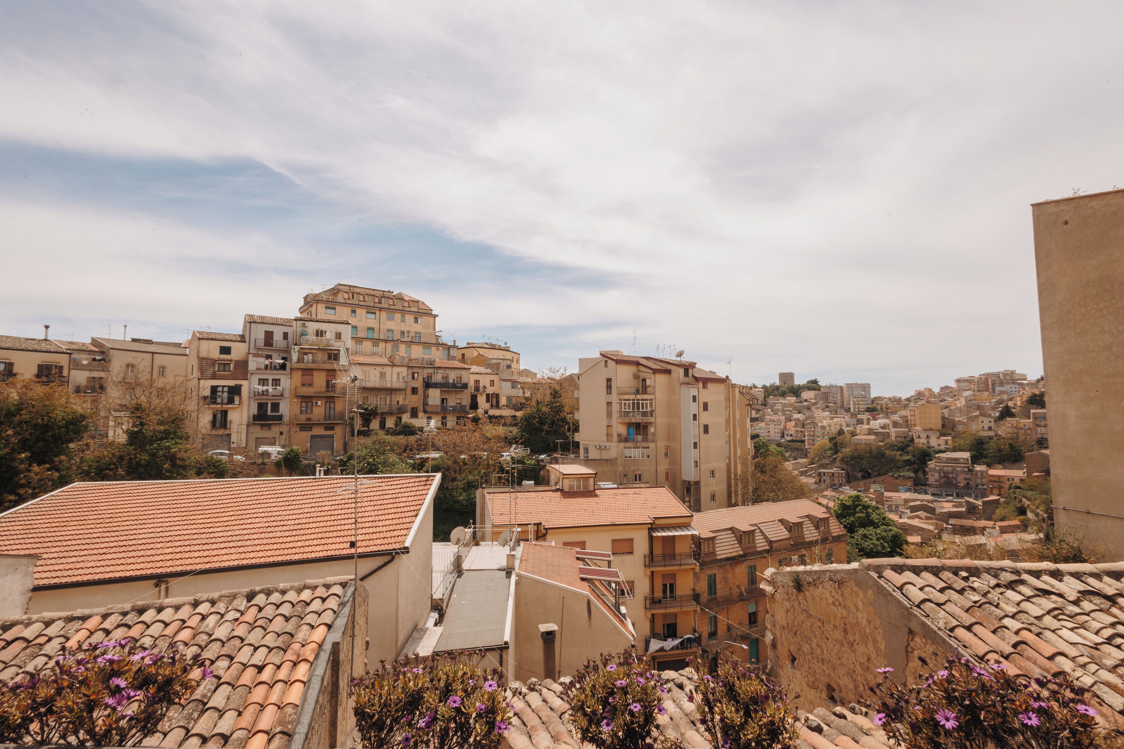Vista di una zona urbana densamente popolata con edifici dalle tegole color terracotta, alcuni con balconi, sotto un cielo parzialmente nuvoloso.