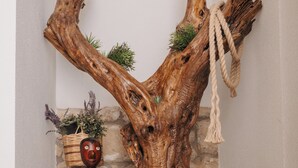 Une sculpture rustique en bois, ornée d’une corde, un panier tressé contenant des plantes et une petite plante en pot, posée sur une étagère.