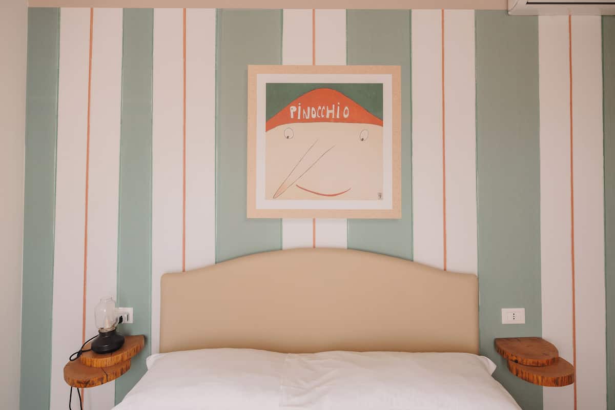 A bedroom with a striped wall, a framed picture of a cartoon character, a bed, and two wooden nightstands with lamps.