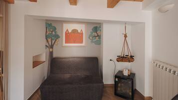 A cozy room with a dark-colored sofa, a wooden ceiling, a framed picture, and a hanging basket.