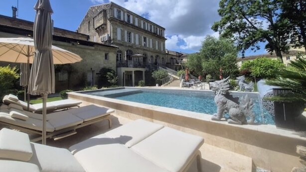 Un espace piscine avec des chaises longues, une statue et un bâtiment en arrière-plan.